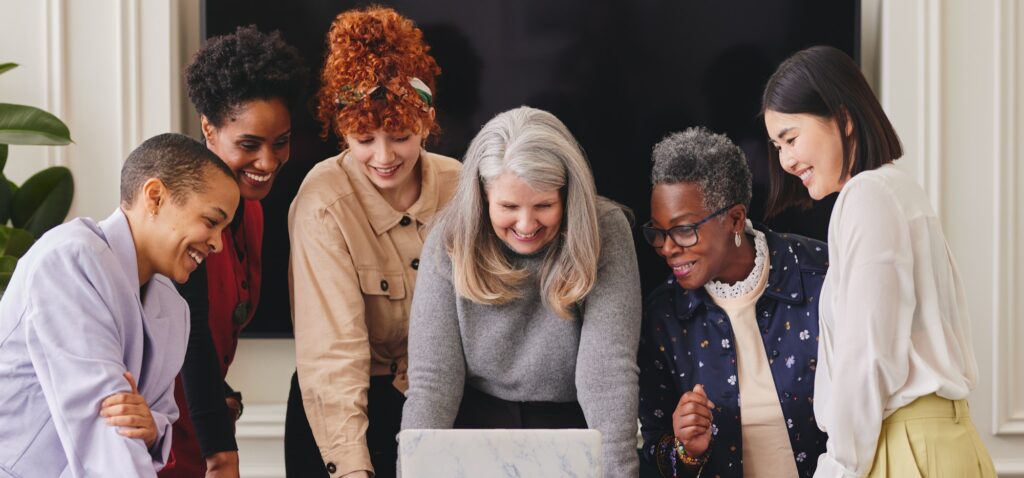 Portrait of cheerful multiethnic women in business meeting looking at laptop and smiling