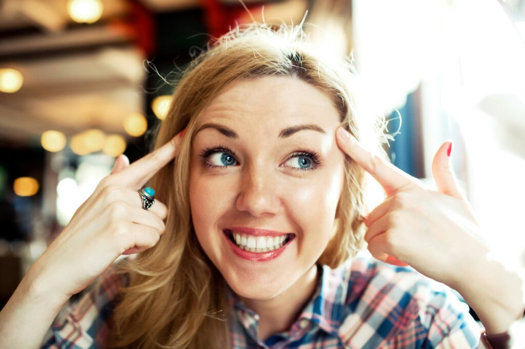 Young smiling positive thinking successful woman pointing finger to her head.